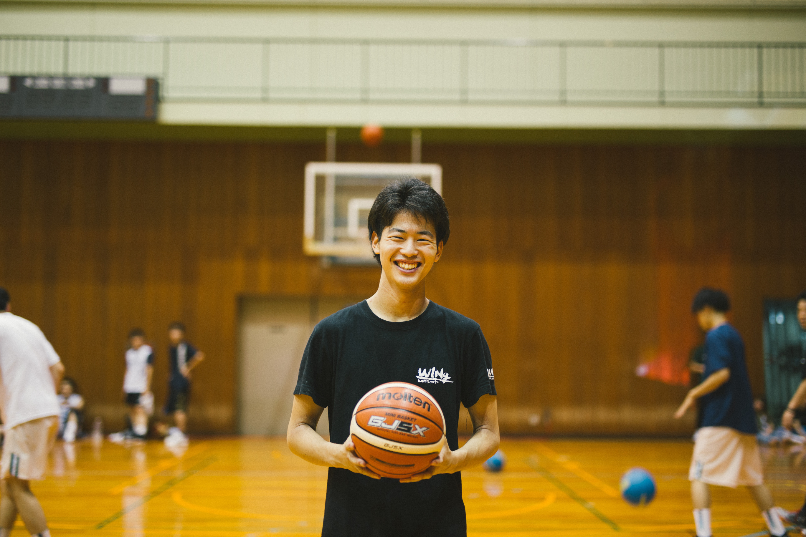 体育館でバスケットボールを笑顔で持つ青年。